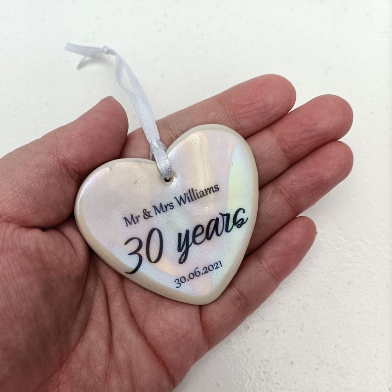 May include: White ceramic heart ornament with iridescent finish. It has the text "Mr & Mrs Williams 30 years 30.06.2021" printed on it.