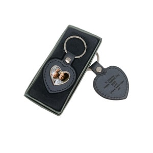 May include: Black leather heart-shaped keyring with a photo insert and a silver key ring. The keyring also includes a second heart-shaped charm with the inscription "To Mummy Happy Mother's Day 2023 Love Olivia & Amelia xxx"