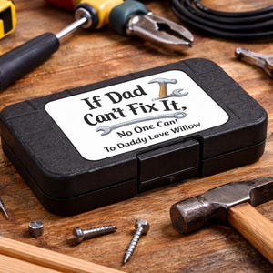 May include: A black toolbox with the text "If Dad Can't Fix It, No One Can! To Daddy Love Willow" on a white label. The toolbox is surrounded by tools, including a hammer, pliers, and screws, all on a wooden surface.