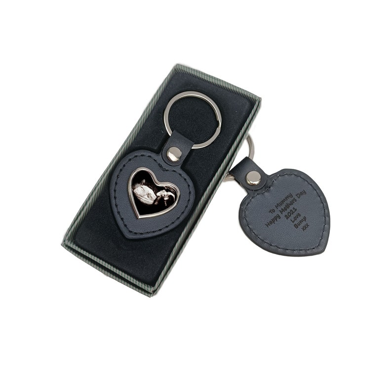 May include: A black leather heart-shaped keyring with a silver frame holding a photo. The keyring has a silver ring and a smaller black leather heart-shaped tag with the text "To Mummy Happy Mother's Day 2023 Love Bump xxx".