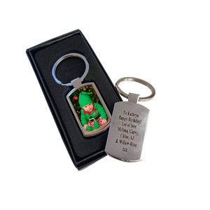 A silver photo keyring in a black gift box with a printed image of a baby in a green Christmas elf outfit. Next to it is the back of another keyring engraved with a birthday message addressed to Kathryn from Melissa, Garry, Chloe, AJ, and Willow-Rose.