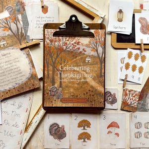 May include: A wooden clipboard displays a print titled Celebrating Thanksgiving, surrounded by educational cards featuring illustrations of turkeys, squirrels, mushrooms, and pumpkins, alongside sheets with cursive alphabet letters and harvest hymns.