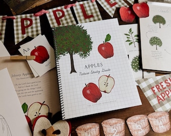 May include: A collection of apple-themed educational materials. Includes a spiral-bound "Apples Nature Study Guide", flashcards, and decorative elements. The guide features illustrations of apples and trees. A gingham banner spells "APPLES".