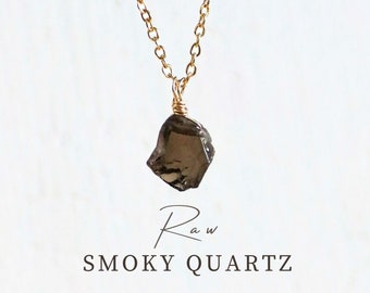 May include: A gold chain necklace with a raw smoky quartz pendant. The pendant is a natural, irregular shape and has a dark brown color.