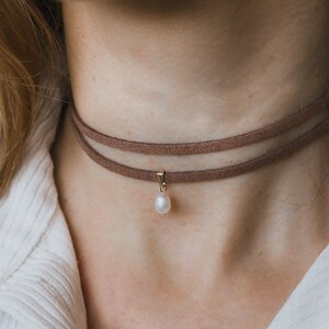 May include: A brown suede choker necklace with a single pearl pendant.