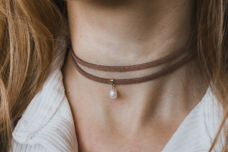 May include: A brown suede choker necklace with a single pearl pendant.