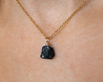 May include: A gold chain necklace with a black, rough-cut gemstone pendant.