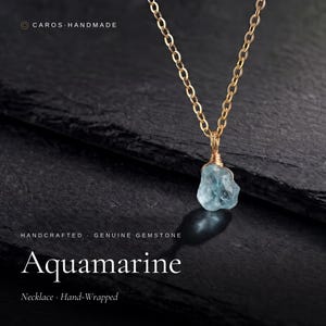 May include: A gold-toned chain necklace featuring a raw, light blue aquamarine gemstone pendant. The stone is secured with hand-wrapped gold-toned wire. Text on the image includes CAROS HANDMADE, HANDCRAFTED, GENUINE GEMSTONE, Aquamarine, and Necklace Hand-Wrapped.