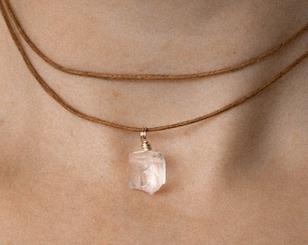May include: A simple, layered brown cord necklace with a clear, faceted crystal pendant.