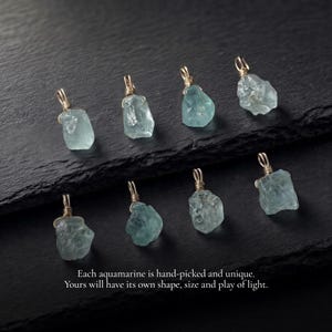 May include: Eight raw, light blue aquamarine pendants, each wrapped in gold-colored wire with a small loop at the top. The text reads: Each aquamarine is hand-picked and unique. Yours will have its own shape, size and play of light.