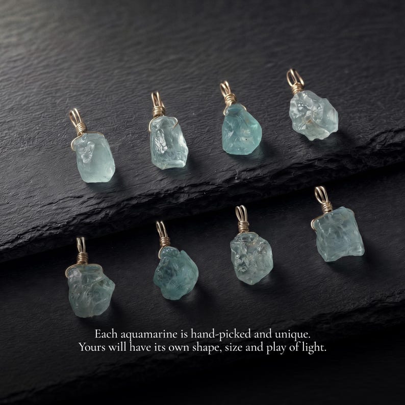 May include: Eight raw, light blue aquamarine pendants, each wrapped in gold-colored wire with a small loop at the top. The text reads: Each aquamarine is hand-picked and unique. Yours will have its own shape, size and play of light.