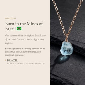May include: A raw, light blue aquamarine gemstone pendant suspended from a delicate gold-toned metal chain. The stone features an irregular, natural shape and is secured by a wire-wrapped setting. The text reads: ORIGIN Born in the Mines of Brazil.