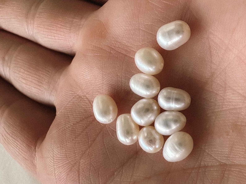 May include: A collection of white oval-shaped pearls in a hand.