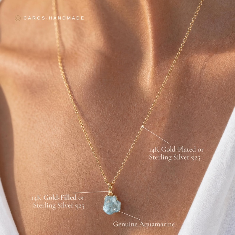 May include: A gold-colored chain necklace featuring a raw, light blue genuine aquamarine pendant. The text on the image indicates options for 14K gold-plated, 14K gold-filled, or sterling silver 925 materials for the chain and pendant setting.