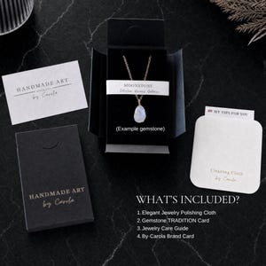 May include: A necklace with a teardrop-shaped moonstone pendant on a thin chain, presented in a black box. Includes a white card labeled HANDMADE ART by Carola, a cleaning cloth labeled MY TIPS FOR YOU, and a list detailing the included items.