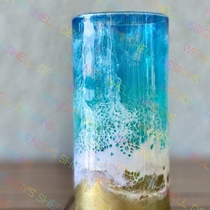 Puede incluir: Un vaso de vidrio transparente con un dise&ntilde;o inspirado en el oc&eacute;ano azul, verde y blanco. La parte inferior del vaso est&aacute; pintada de oro.