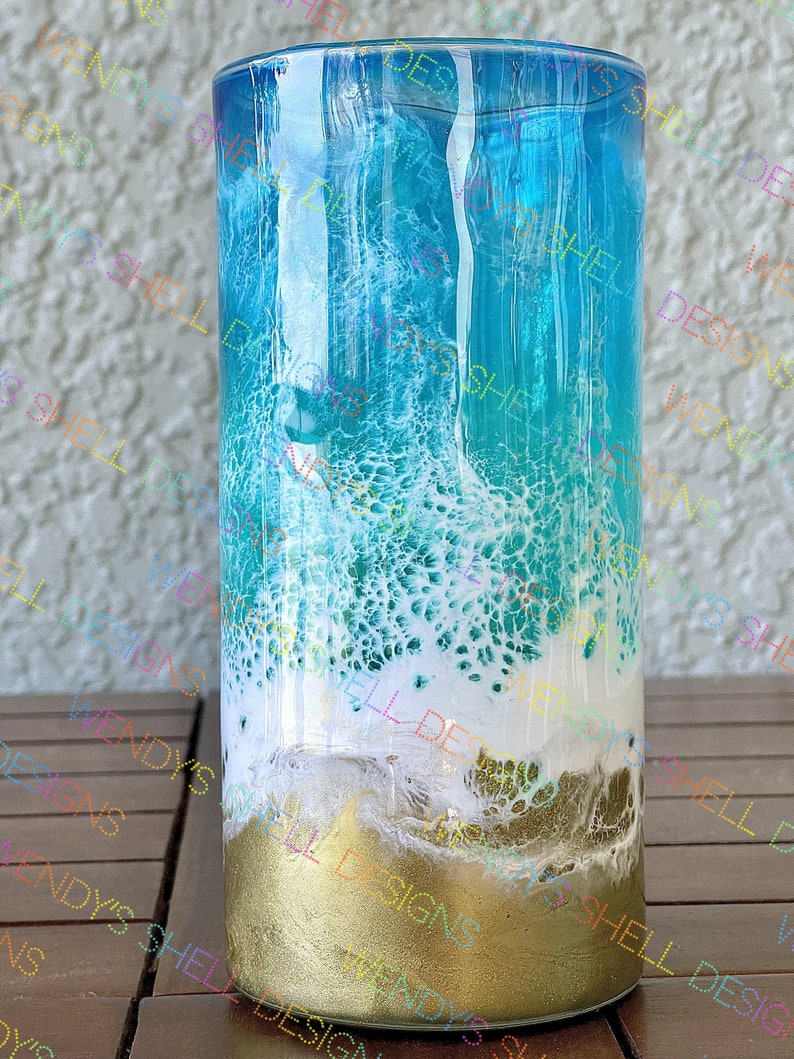 Puede incluir: Un vaso de vidrio transparente con un dise&ntilde;o de ola de oc&eacute;ano azul, blanco y dorado. El vaso est&aacute; lleno de un l&iacute;quido azul y tiene un borde blanco.