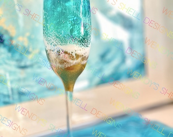 May include: A champagne flute with a blue and gold design. The glass is filled with a white liquid and has a textured surface. The glass is sitting on a blue surface.