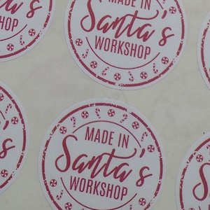 May include: Four round white stickers with a red border and red text that reads "Made in Santa's Workshop" with candy cane and swirl designs around the border.