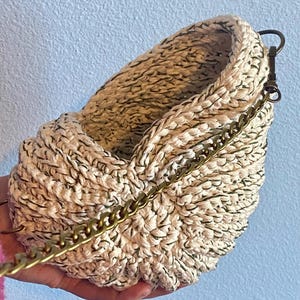 May include: A cream-colored crocheted hanging planter with a gold chain. The planter has a textured, woven design.