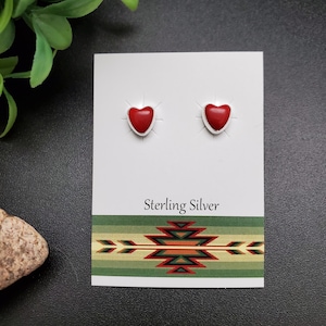 May include: A pair of sterling silver heart-shaped earrings with red stone insets. The earrings are displayed on a white card with the text "Sterling Silver" printed on it.