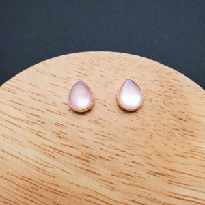 May include: A pair of teardrop-shaped earrings with a pink iridescent finish and gold settings.
