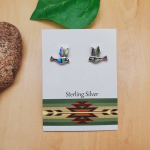 May include: A pair of sterling silver earrings featuring a small bird design with abalone shell inlay. The earrings are displayed on a white card with the text "Sterling Silver".