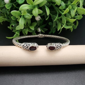 May include: A silver bangle bracelet with a twisted design and two red gemstone accents.