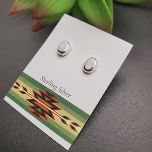 May include: A pair of sterling silver earrings with oval-shaped opal stones. The earrings are displayed on a white card with the words "Sterling Silver" printed on it.