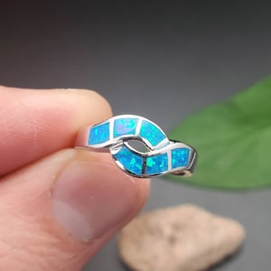 May include: A silver ring with a blue opal stone design. The ring is set in a wave-like pattern.