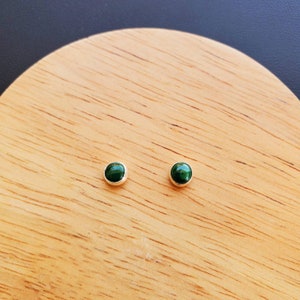 May include: A pair of small, round, green gemstone earrings with silver settings.