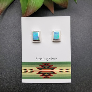 May include: A pair of sterling silver earrings with blue opal square stones. The earrings are displayed on a white card with the text "Sterling Silver".