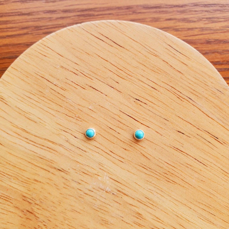 May include: A pair of small, round turquoise stud earrings on a wooden surface.