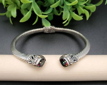 May include: A silver bangle bracelet with a twisted design and two iridescent gemstones set in gold.