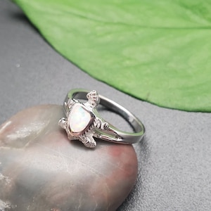 May include: A silver ring with a white opal turtle design.
