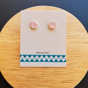 May include: A pair of sterling silver stud earrings with pink gemstone accents. The earrings are displayed on a white card with the text "Sterling Silver".
