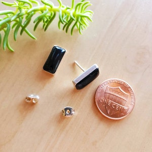 May include: A pair of black onyx earrings with sterling silver posts. The earrings are rectangular in shape and are about the size of a US penny.