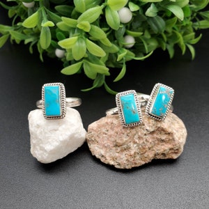 May include: Three silver rings with turquoise stones. The stones are rectangular and have a light blue color. The rings are set on a rock background.