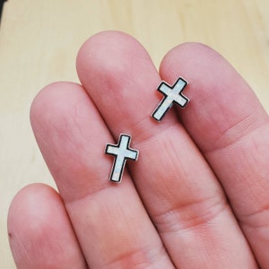 May include: A pair of silver cross earrings with white opal inlays. The earrings are small and delicate.