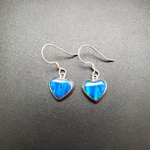 May include: A pair of silver heart-shaped earrings with blue opal stones.