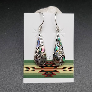 May include: A pair of silver dangle earrings with iridescent abalone shell inlays. The earrings are teardrop shaped and have a beaded border.