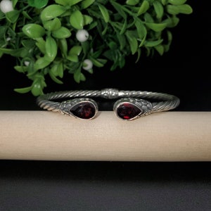 May include: A silver bangle bracelet with a twisted design and two red gemstone accents.