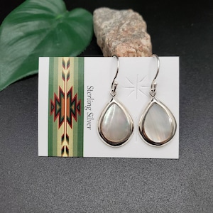May include: Sterling silver teardrop earrings with white mother of pearl inlays. The earrings are on a white card with the text "Sterling Silver" printed on it.