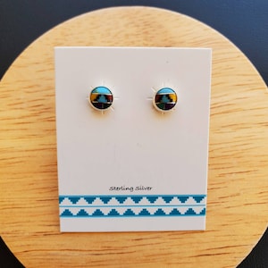 May include: A pair of sterling silver stud earrings with a turquoise and multi-colored inlay design. The earrings are displayed on a white card with the text "Sterling Silver".