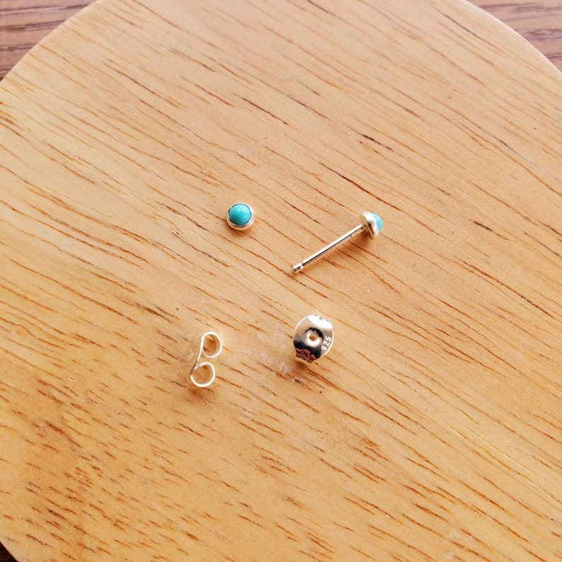 May include: A pair of silver stud earrings with turquoise stones. The earrings are shown on a wooden surface.