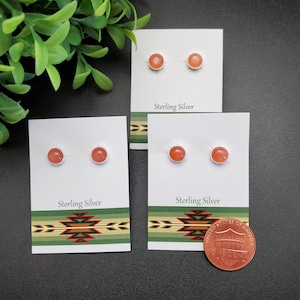May include: Three pairs of sterling silver earrings with orange gemstone cabochons. The earrings are displayed on white cards with the text "Sterling Silver". A penny is included for size reference.