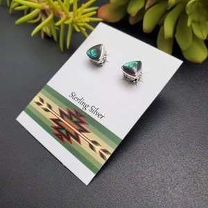 May include: A pair of sterling silver earrings with a triangular abalone shell inlay. The earrings are displayed on a white card with the text "Sterling Silver".