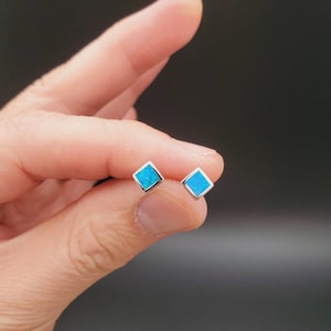 May include: A pair of silver stud earrings with square blue opal stones.