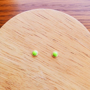 May include: A pair of small, round, lime green stud earrings. The earrings are set in silver.