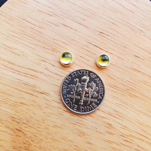 May include: A pair of silver stud earrings with yellow glass stones. The earrings are shown next to a US dime for size comparison.